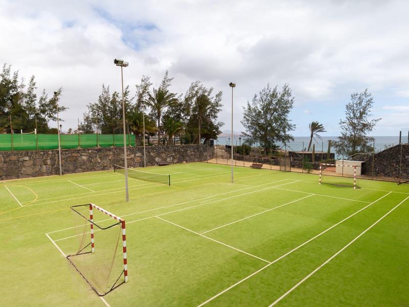 Campo da tennis vuoto con superficie verde e muro circostante sotto cielo nuvoloso