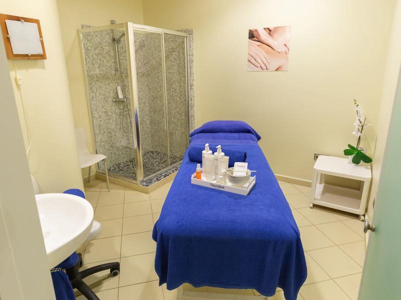 Sala trattamento con lettino blu, doccia e piccolo scaffale per prodotti benessere o medici.