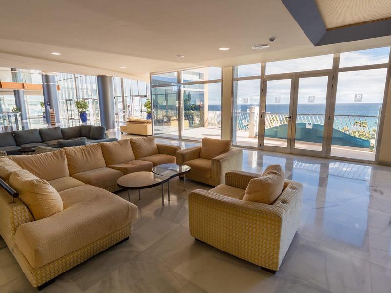 Luminoso salotto con divani beige, porte a vetri e vista mare in un hotel