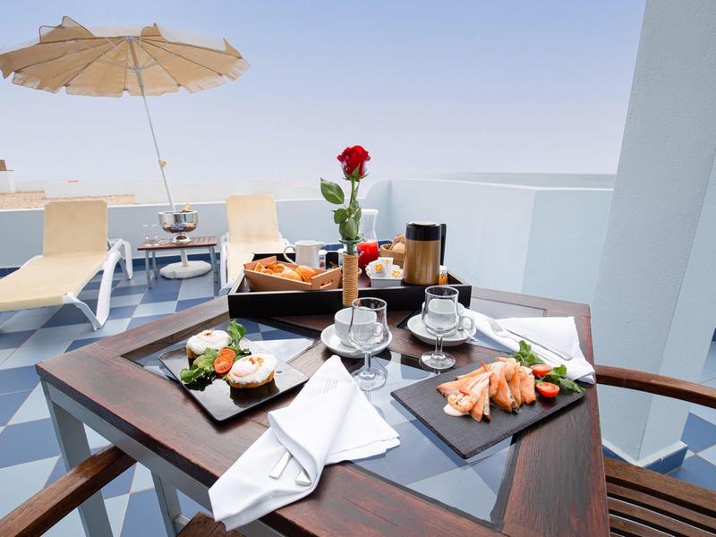 Terrazza con tavolo, colazione con croissant, caffè e una rosa, lettini e ombrellone.