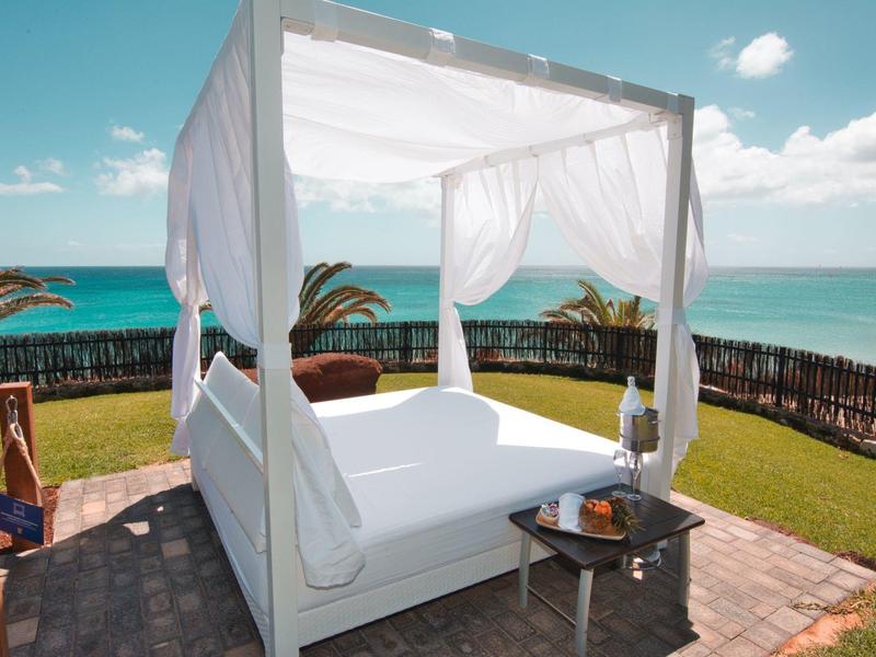 Letto a baldacchino bianco con tende trasparenti su una terrazza con vista sul mare.