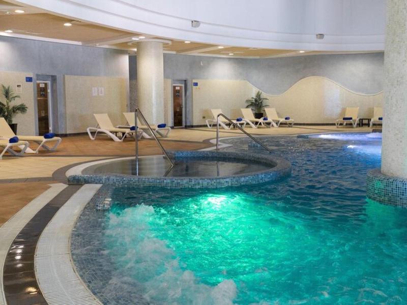 Piscina interna con vasca idromassaggio, sedie a sdraio e illuminazione soffusa in un hotel.