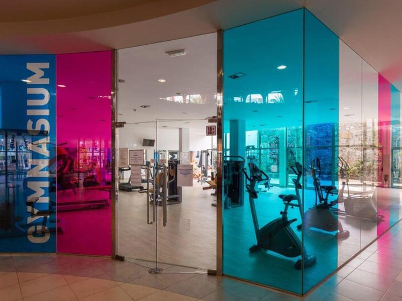 Area palestra moderna con pareti di vetro rosa acceso e blu nell'hotel.