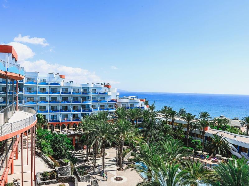 Vista di un hotel moderno con palme e mare sullo sfondo sotto il sole.