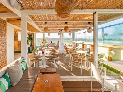 Helles Restaurant mit Holzdach, weißem Mobiliar und großen Fenstern mit Meerblick.