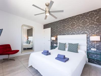 Modern eingerichtetes Schlafzimmer mit Doppelbett, Akzentwand und rotem Sessel.