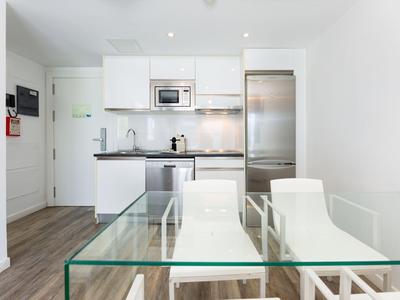 Moderne Küchenecke mit Glas-Tisch und weißen Stühlen in einem hellen Wohnraum