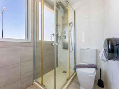 Helles Badezimmer mit Duschkabine, weißer Toilette und grauen Fliesen.