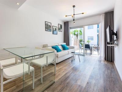 Bright living room with glass dining table, sofa, and balcony access with garden view.