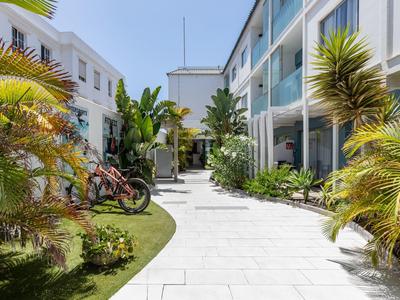 Hotel courtyard with white flooring, plants, and modern architecture under sunny weather