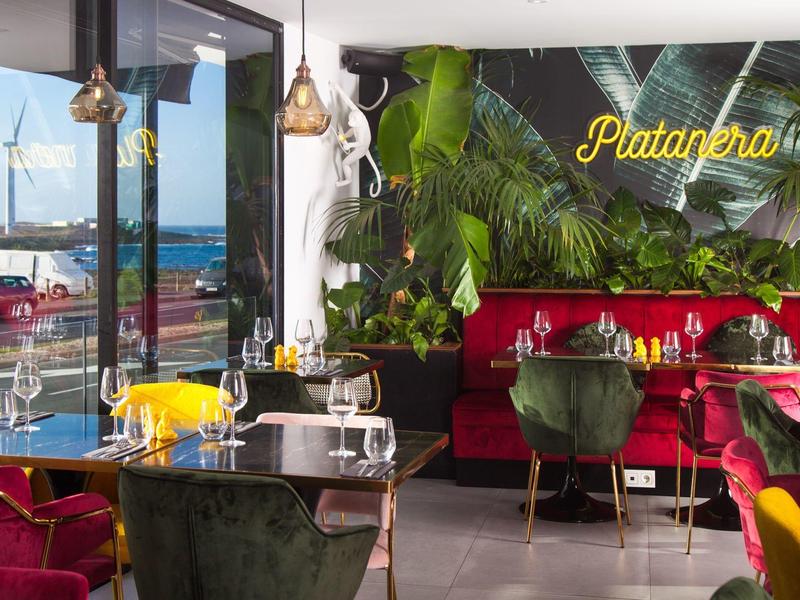 Modern restaurant with colorful chairs and harbor view through large windows.