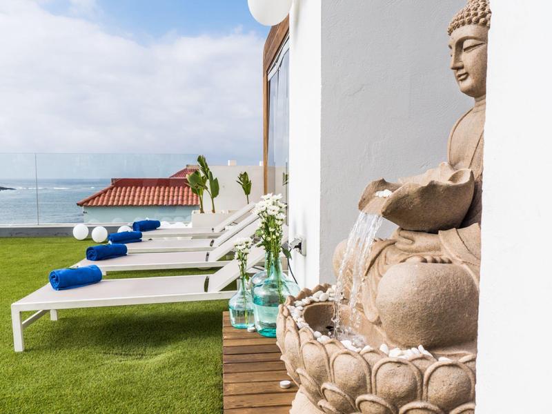 Modern outdoor area with sun loungers, Buddha statue, and ocean view.