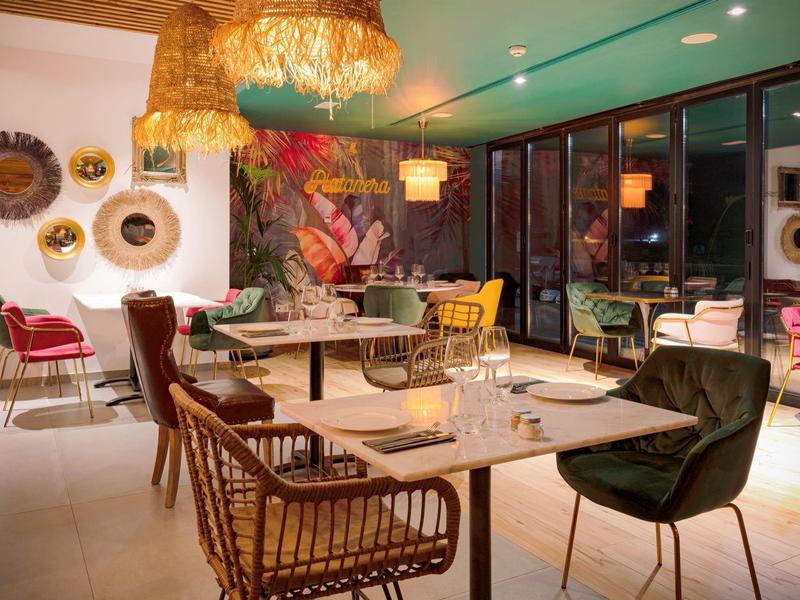 Modern restaurant with colorful furniture and cozy chairs next to large windows.