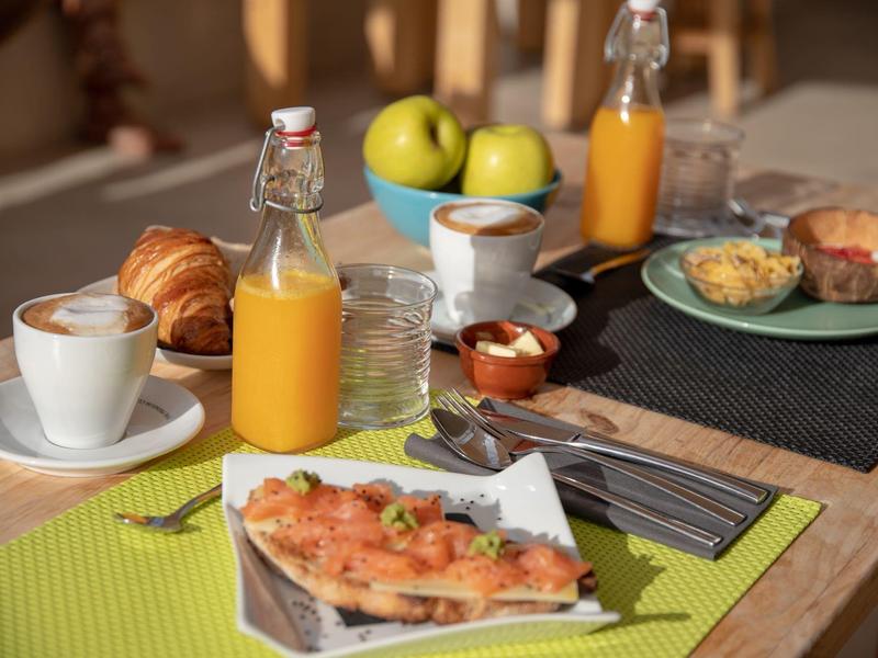 Breakfast table with coffee, croissants, orange juice, and fresh pastries in a cozy setting.