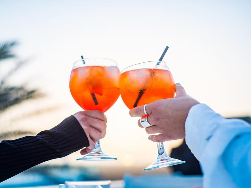 Two hands clinking large glasses with orange cocktails, blurred background.