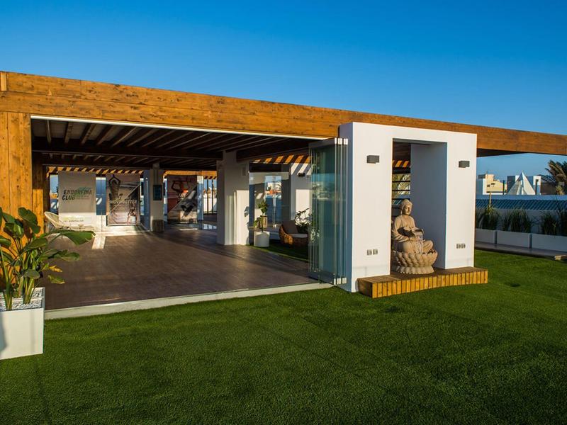 Modern hotel pavilion with open design, wood cladding, and sculpture in front of green lawn.