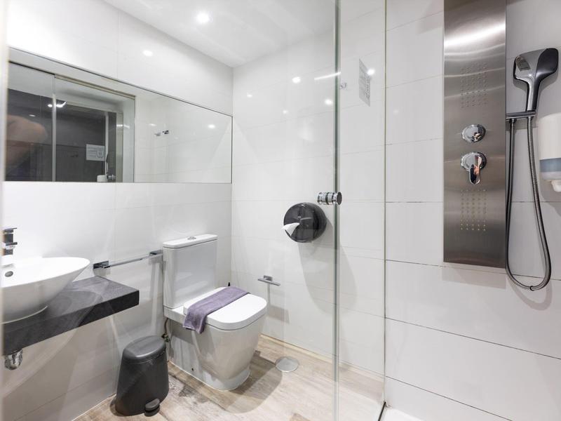 Modern bathroom with shower, toilet, sink, and large mirror in white and gray.