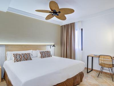 Camera d'hotel luminosa con letto grande, ventilatore a soffitto e scrivania vicino alla finestra.