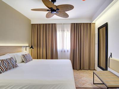 Camera d'hotel luminosa con letto matrimoniale, ventilatore a soffitto e finestra con tende marroni