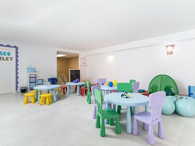 Sala giochi luminosa con tavoli, sedie colorate e giochi per bambini in un hotel.