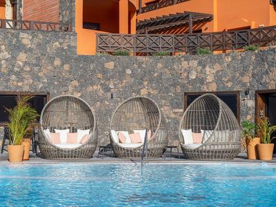 Tre poltrone rotonde in vimini grigio con cuscini accanto a una piscina davanti a un muro di pietra.