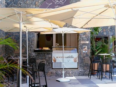 Area salotto con ombrelloni davanti a un ristorante con pareti in pietra e tavoli.