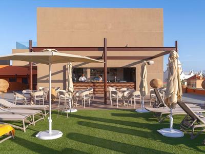 Terrazza sul tetto con lettini, ombrelloni e zona salotto davanti alla facciata dell'edificio sotto un cielo sereno