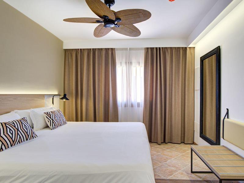 Camera d'hotel luminosa con letto matrimoniale, ventilatore a soffitto e finestra con tende marroni