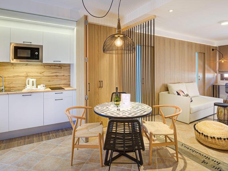 Area soggiorno moderna con angolo cottura, tavolo da pranzo e divano accogliente in toni caldi.