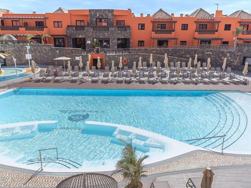 Grande piscina dell'hotel con sedie a sdraio e edificio rosso di due piani sullo sfondo