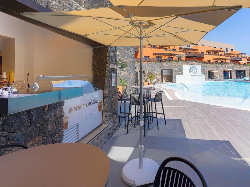 Area piscina con bar, ombrellone e sedie accanto a una piscina all'aperto in un complesso alberghiero.