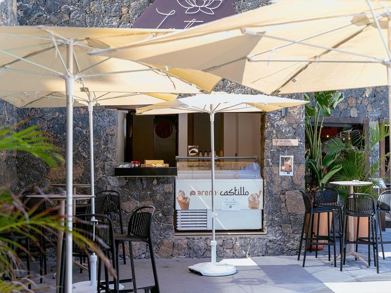 Area salotto con ombrelloni davanti a un ristorante con pareti in pietra e tavoli.