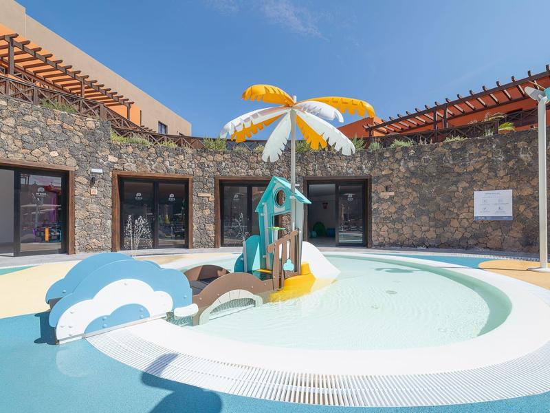 Piscina per bambini con ombrellone colorato e giochi in un hotel.