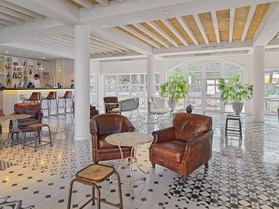 Salon d'hôtel lumineux avec fauteuils en cuir, grande fenêtre et sol à motifs noir et blanc.