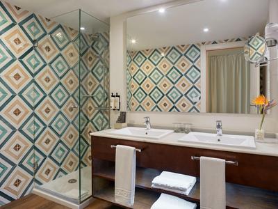 Salle de bain d'hôtel moderne avec lavabos, grands miroirs et cabine de douche aux carreaux colorés.