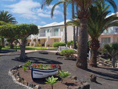Complexe hôtelière avec palmiers, jardin décoratif et allée sous un ciel bleu.