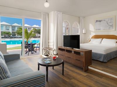Chambre d'hôtel lumineuse avec sol en bois, grande porte vitrée vers la piscine et mobilier moderne.