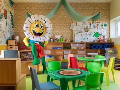 Espace de jeu pour enfants coloré avec table de jeu, chaises et un tournesol en tissu souriant.