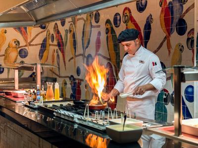 Chef cuisine sur un grill ouvert dans un buffet d'hôtel avec des carreaux muraux colorés.