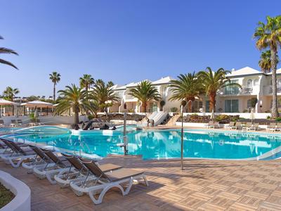 Piscine d'hôtel moderne avec chaises longues et palmiers sous un ciel bleu clair.