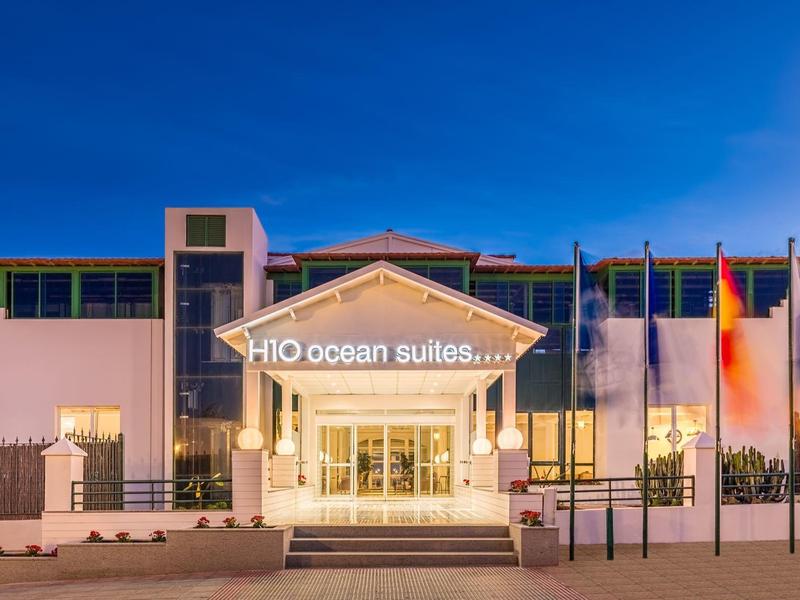 Modern hotel entrance with illuminated sign and flags under clear blue sky at dusk.
