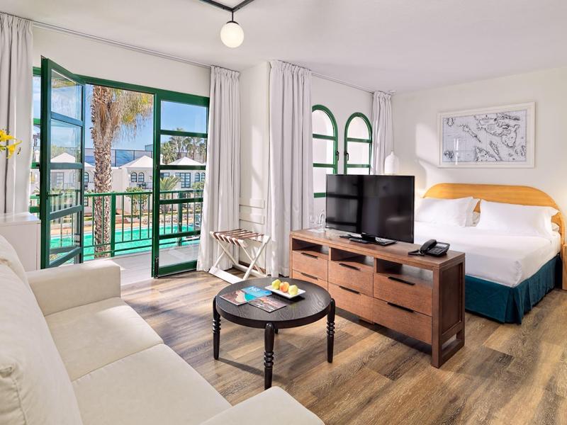 Bright hotel room with a balcony, sea view, modern furniture, and wood flooring.