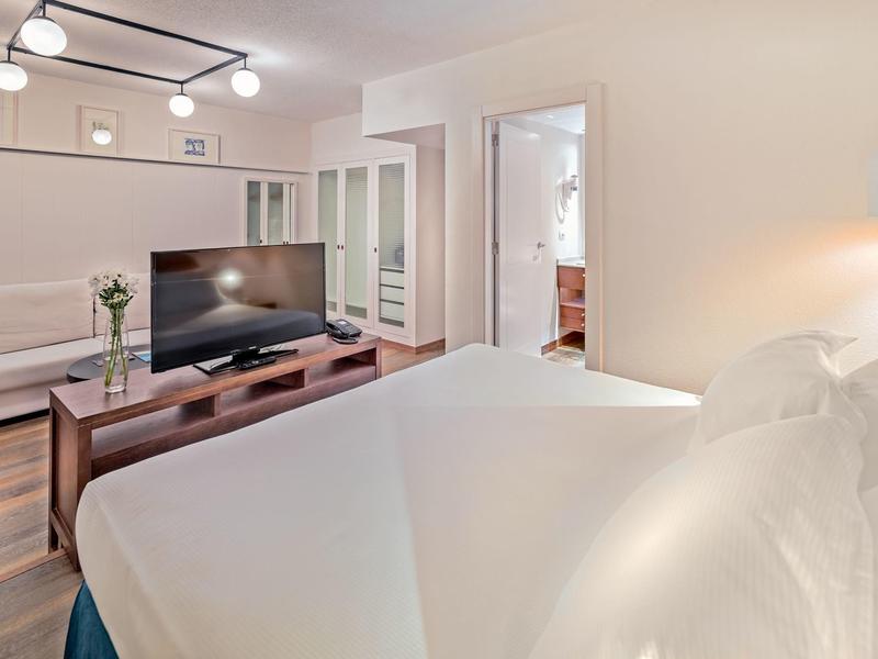 Modern hotel room with bed, TV, sofa, and bright lighting