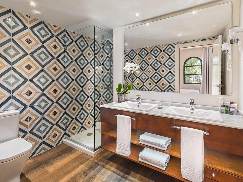 Modern bathroom with geometric wall tiles, wooden vanity, glass shower, and large mirror.