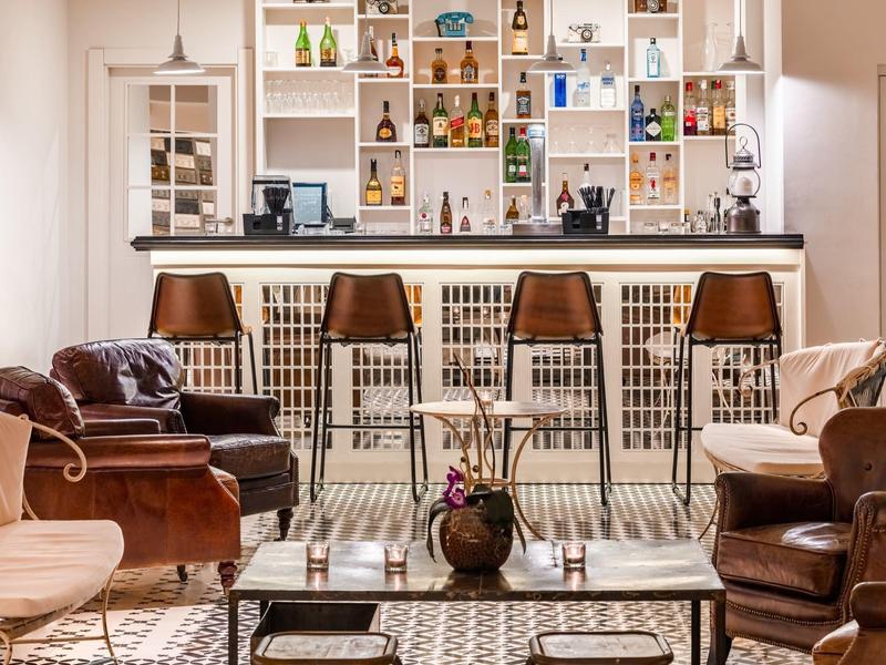 Cozy hotel lounge with leather armchairs, a bar counter, stools, and shelves with bottles and decor.