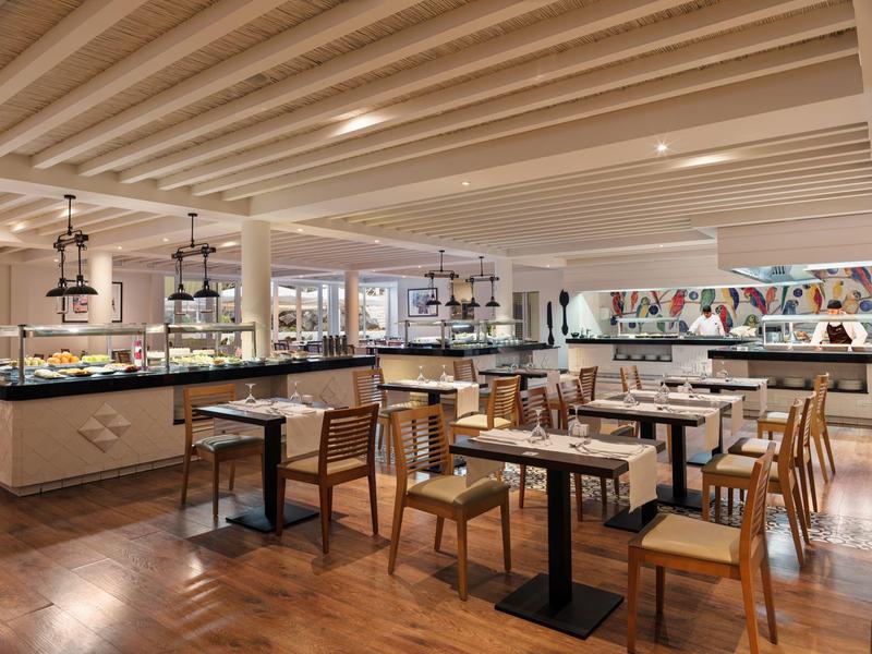 Modern dining area with wooden chairs, tables, and buffet counters under a beamed ceiling.