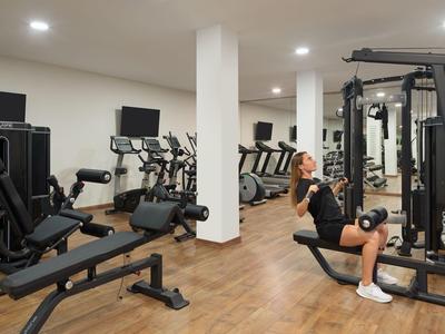 Modern gym with workout machines and two people exercising.