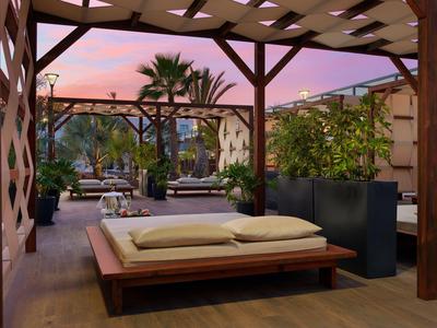 Terrace area with wooden loungers and palm trees under a pink sunset.