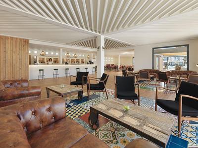Bright hotel lounge with seating areas, wooden accents, and a modern bar area.