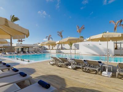 Outdoor hotel pool area with sun loungers and large umbrellas under a clear blue sky.